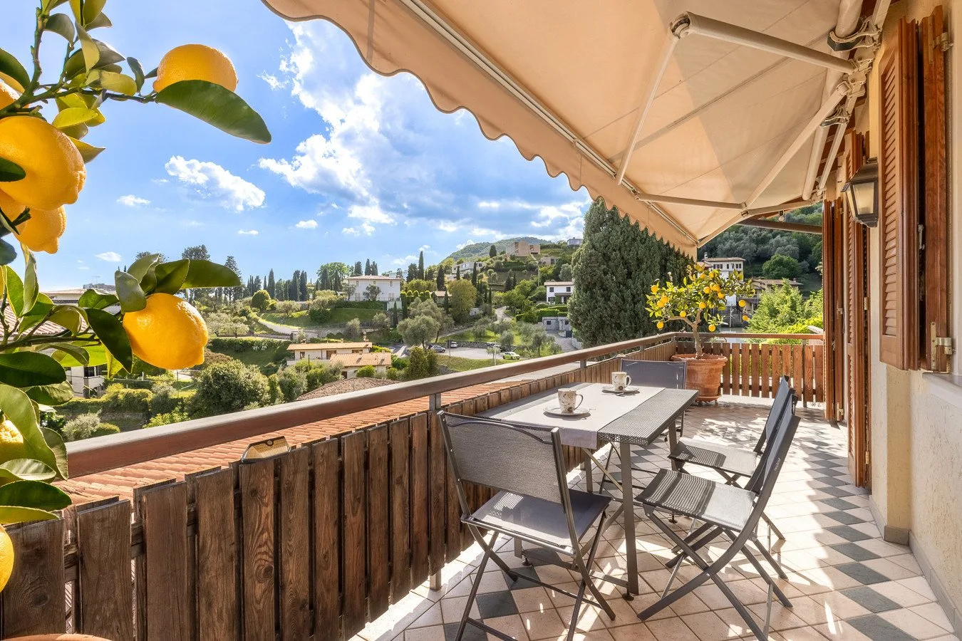 A furnished outdoor terrace overlooks a green hillside beneath a retractable awning.