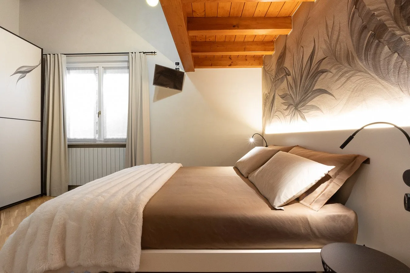 A bedroom with a bed beneath a wooden beam ceiling.