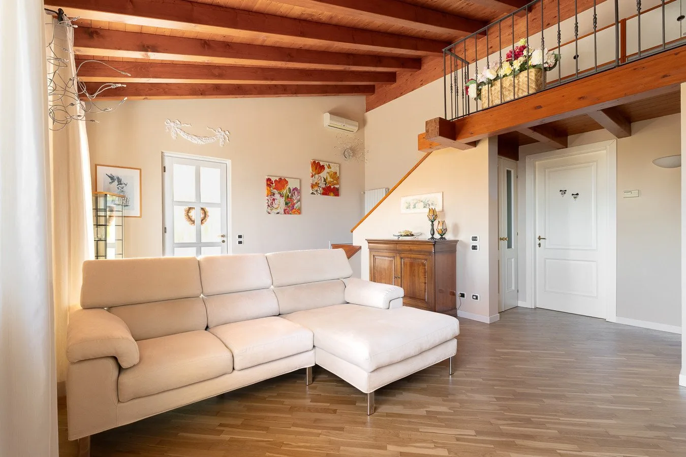 A bright living room with beige seating beneath a wooden mezzanine.