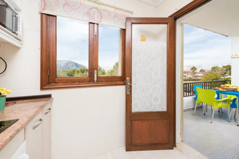 A kitchen opens onto a balcony with colorful seating and views of the hills.