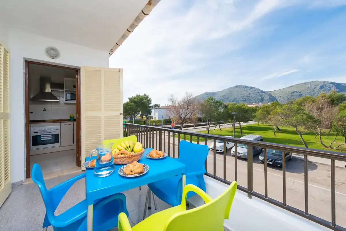 A balcony dining area with bright seating overlooks a road and green park.