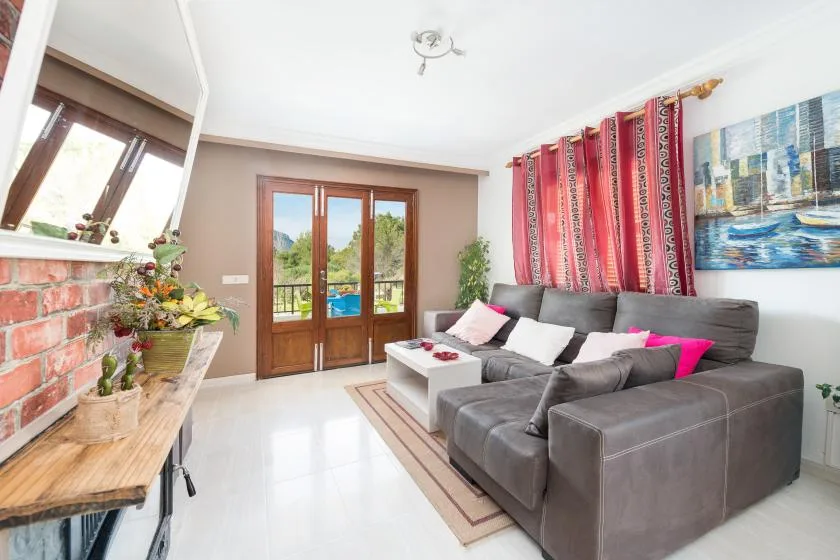 A bright living room with gray seating, red curtains, and doors opening to a balcony.