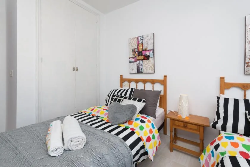A bedroom with two beds, colorful patterned bedding, and a small bedside table.