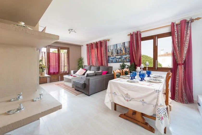 A bright living and dining area has gray seating beside a set table and large windows.