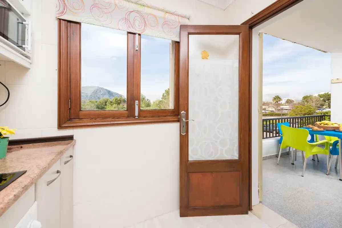 A kitchen opens through a wooden door onto a terrace with colorful seating.