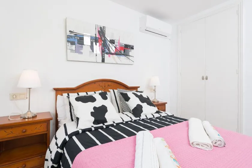 A bedroom with a wooden bed, black-and-white bedding, and a pink cover.
