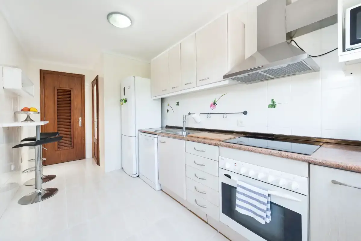 A bright kitchen with white cabinets, a refrigerator, and a counter.