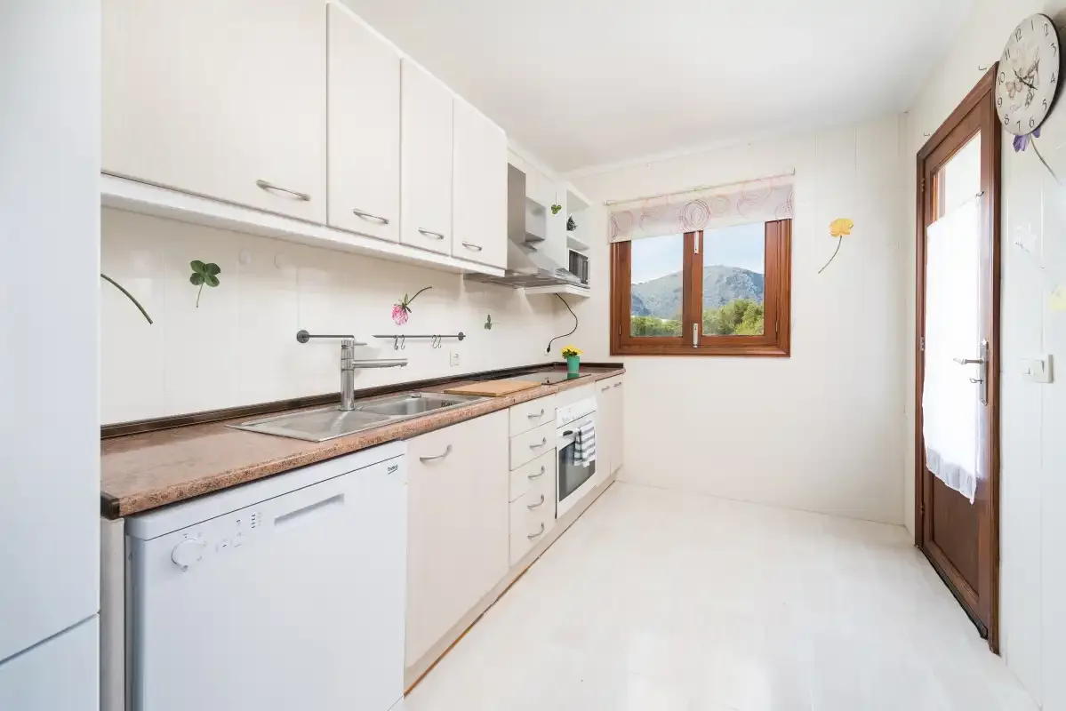 A bright kitchen with white cabinets, a countertop, and a window overlooking hills.