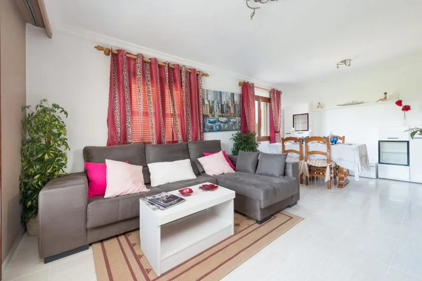 A bright living and dining area with gray seating and red curtains.