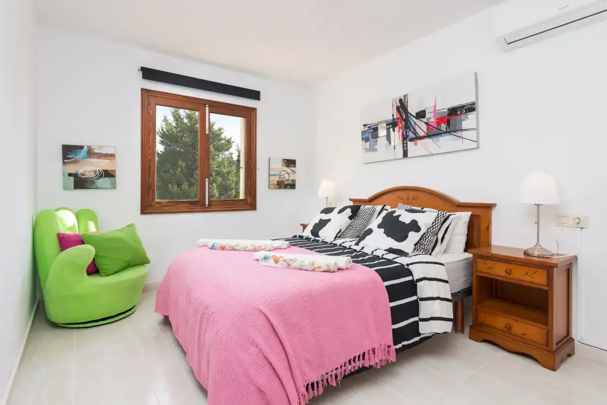 A bedroom with a wooden bed, pink bedspread, and green seating.
