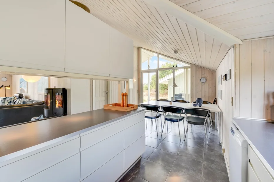 A bright kitchen and dining area with white cabinets, a long counter, and a table by the windows.
