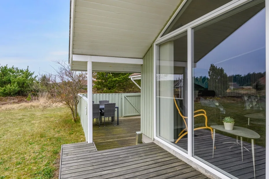 A covered deck with outdoor seating beside large glass doors.