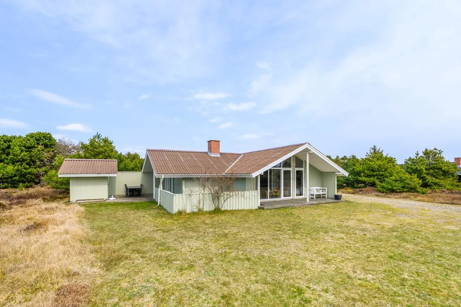 A single-story house stands in an open grassy yard beneath a blue sky.