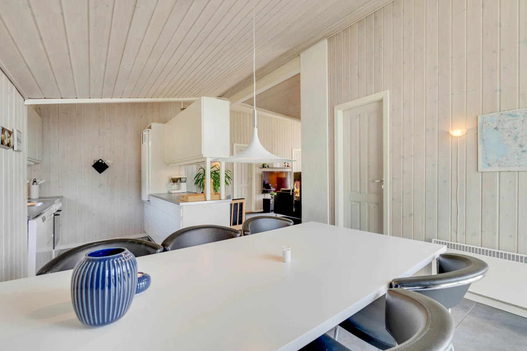 A bright dining area opens onto a kitchen, with a large table in the foreground.