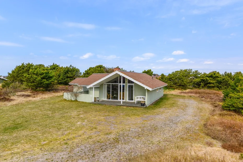A low house stands in an open grassy landscape beneath a blue sky.