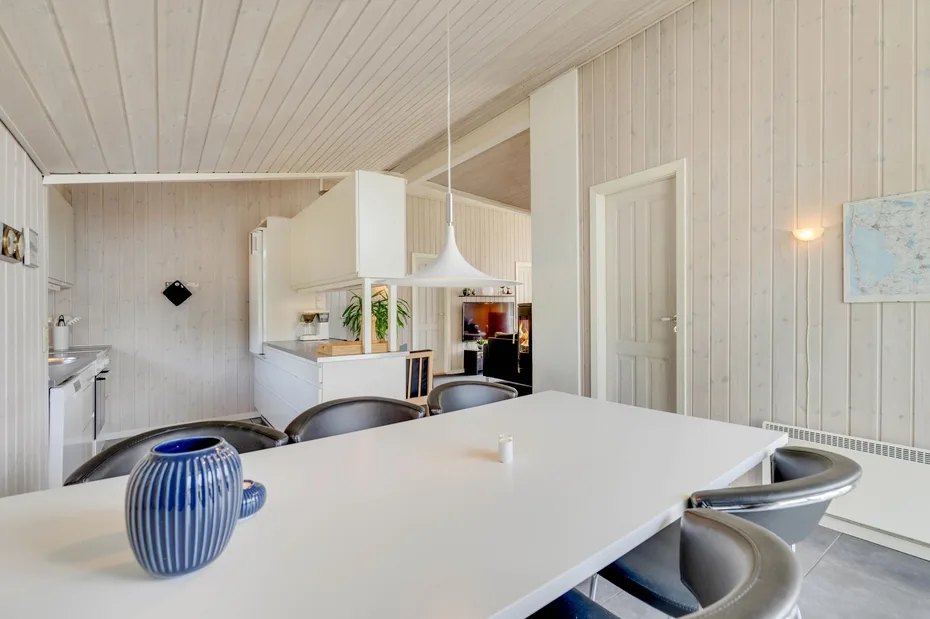 A bright dining area with a large white table and open kitchen.