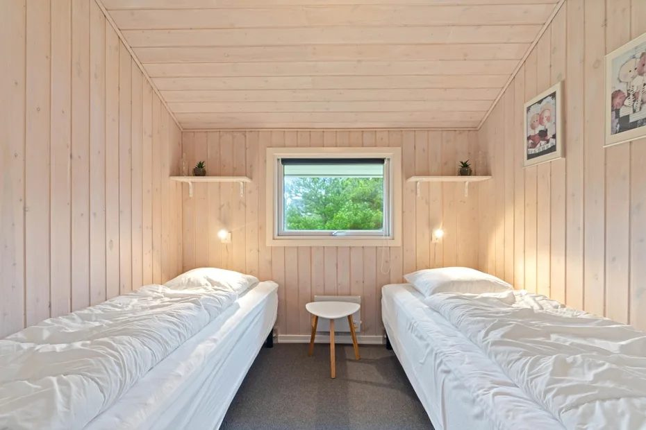 A compact bedroom with two single beds and a window overlooking greenery.