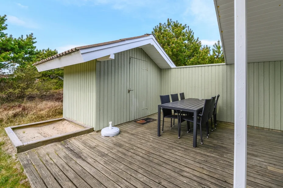 An outdoor wooden deck has a dining table and chairs beside a small shed.
