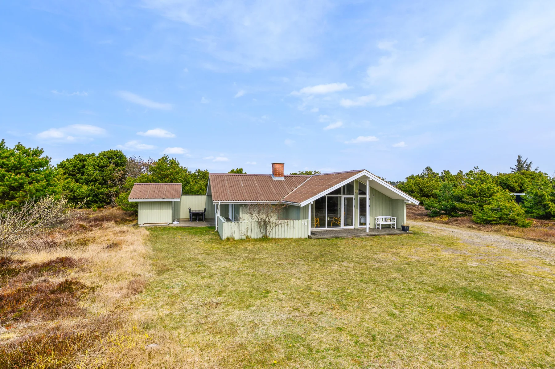 A low house with a sloped roof sits beside a broad grassy yard.