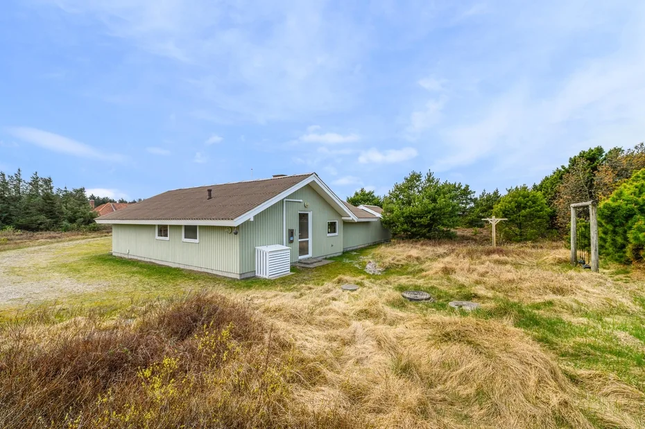 A small house stands in a grassy clearing beneath a blue sky.