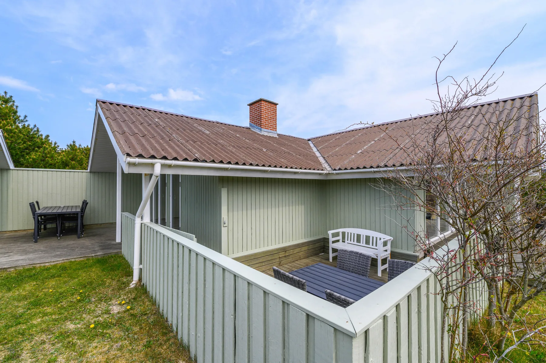 A pale green house with a covered patio and outdoor seating.