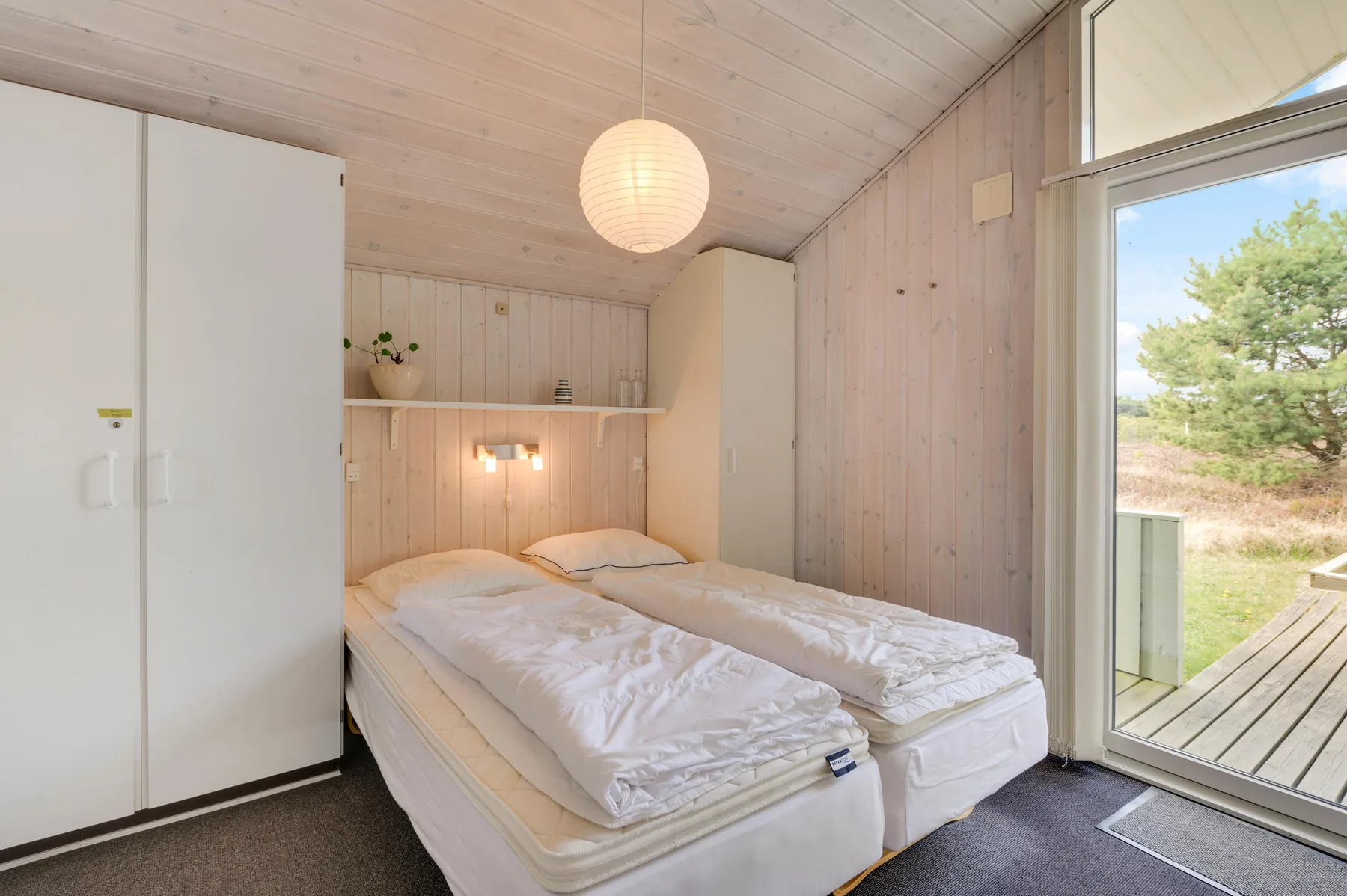 A bedroom with two beds beside a large glass door opening onto a deck.