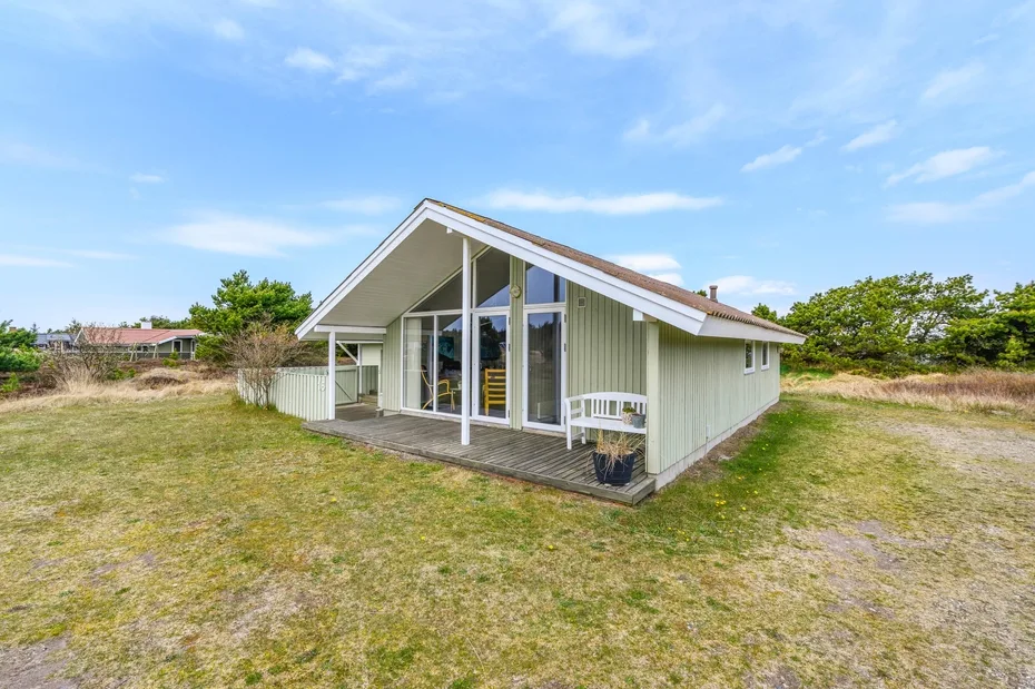 A small house with a glazed front sits in an open grassy yard.