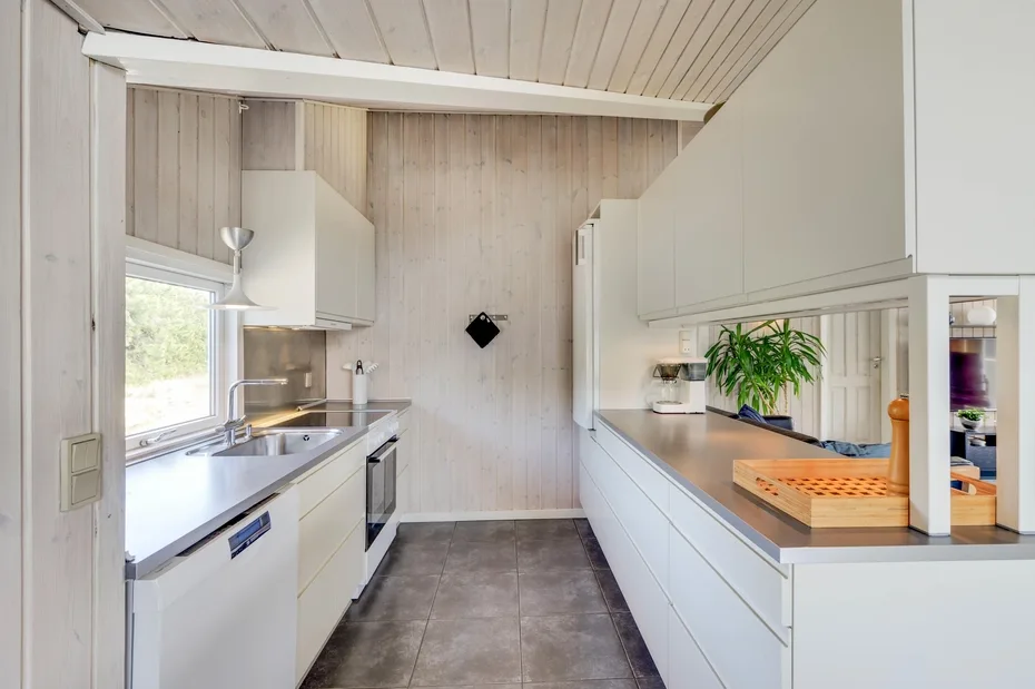 A bright galley kitchen with white cabinets, counters, and a window.