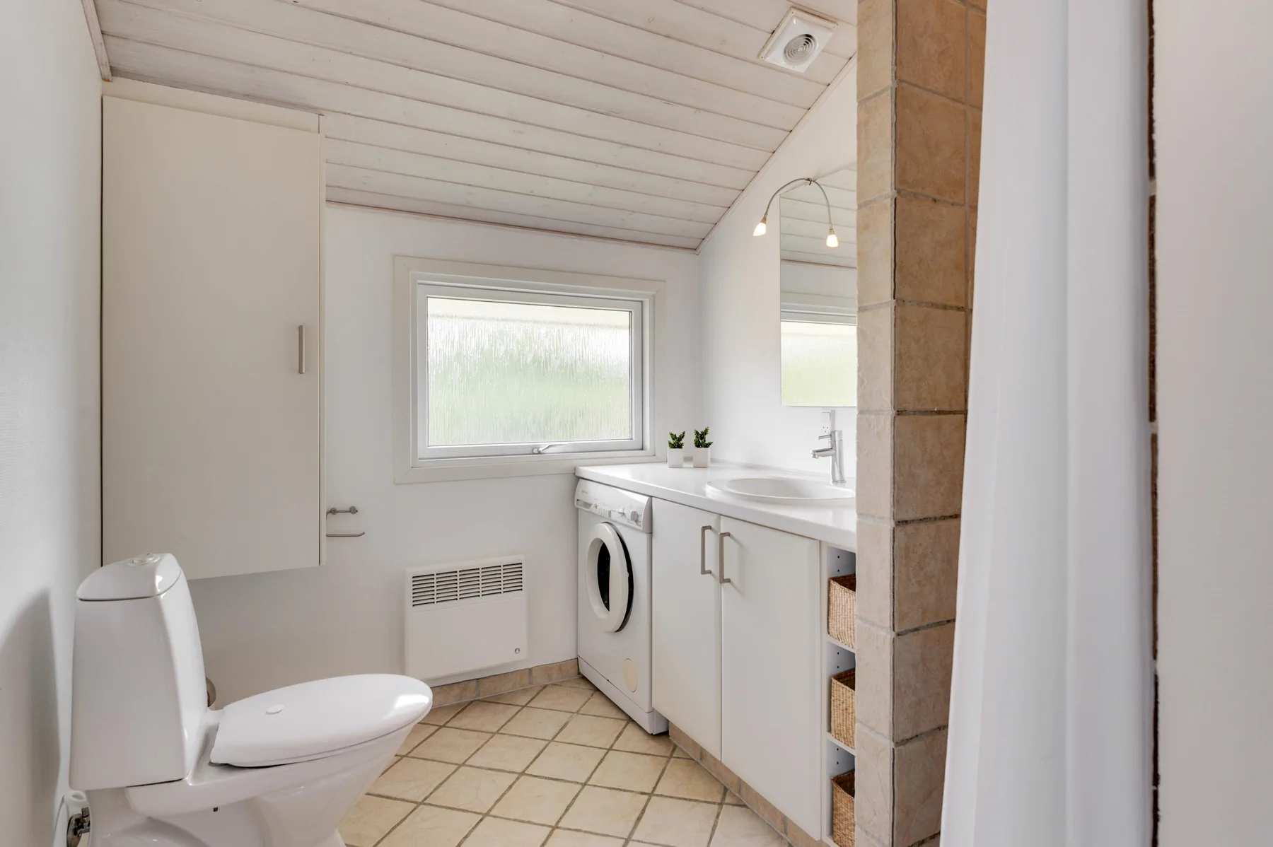 A bright bathroom with a toilet, washing machine, and sink.