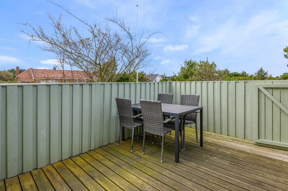 An outdoor deck has a dining table and seating beside a tall fence.