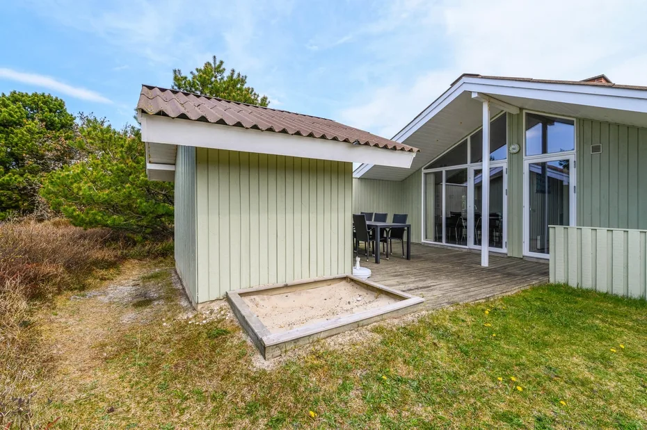 A modern house opens onto a wooden deck and grassy yard.