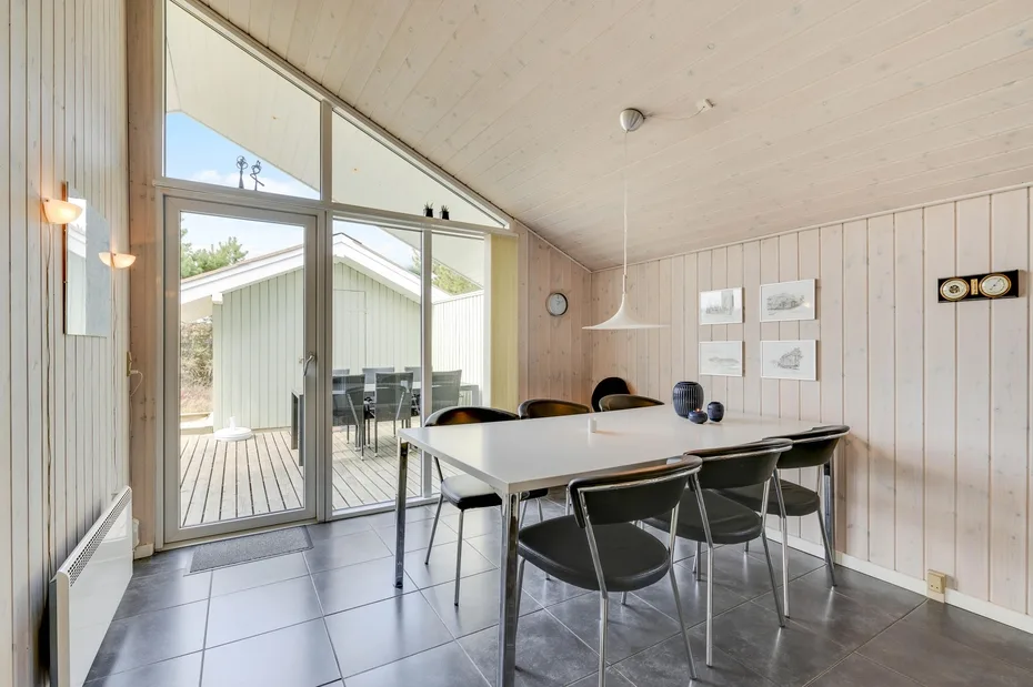 A dining area with a long table and chairs beside large glass doors.