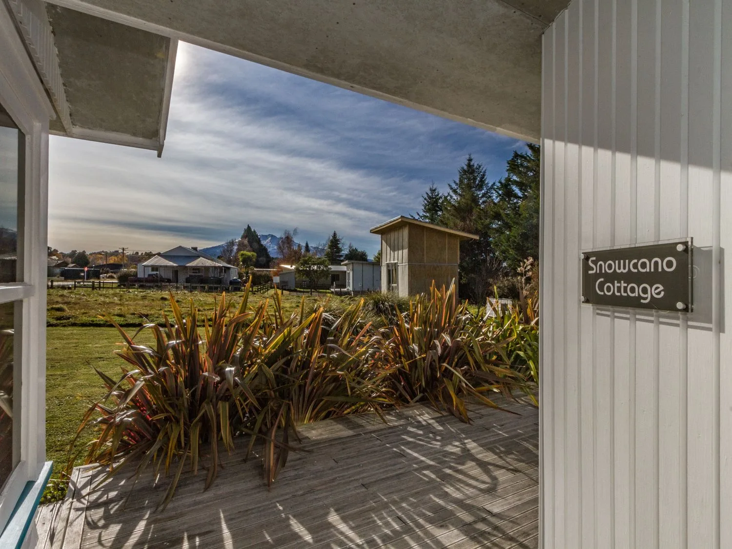 A covered porch overlooks planted landscaping, nearby houses, and distant mountains.