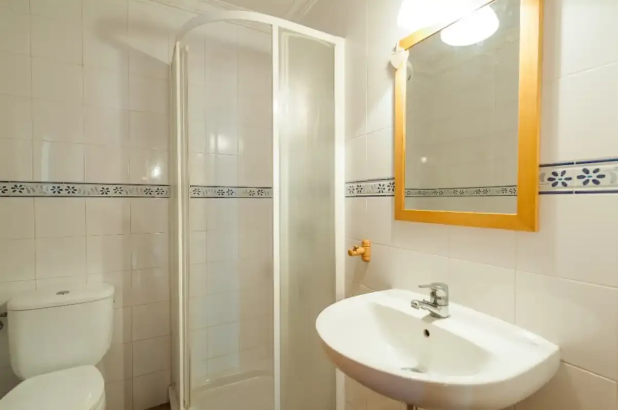 Un baño alicatado con ducha, lavabo y espejo de pared.