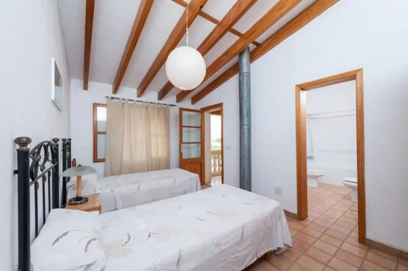 Un dormitorio con dos camas, vigas de madera a la vista y una puerta hacia un baño.