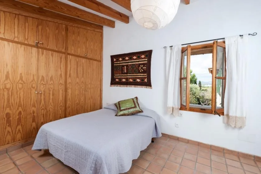 Un dormitorio con una cama, armarios de madera y una ventana abierta.