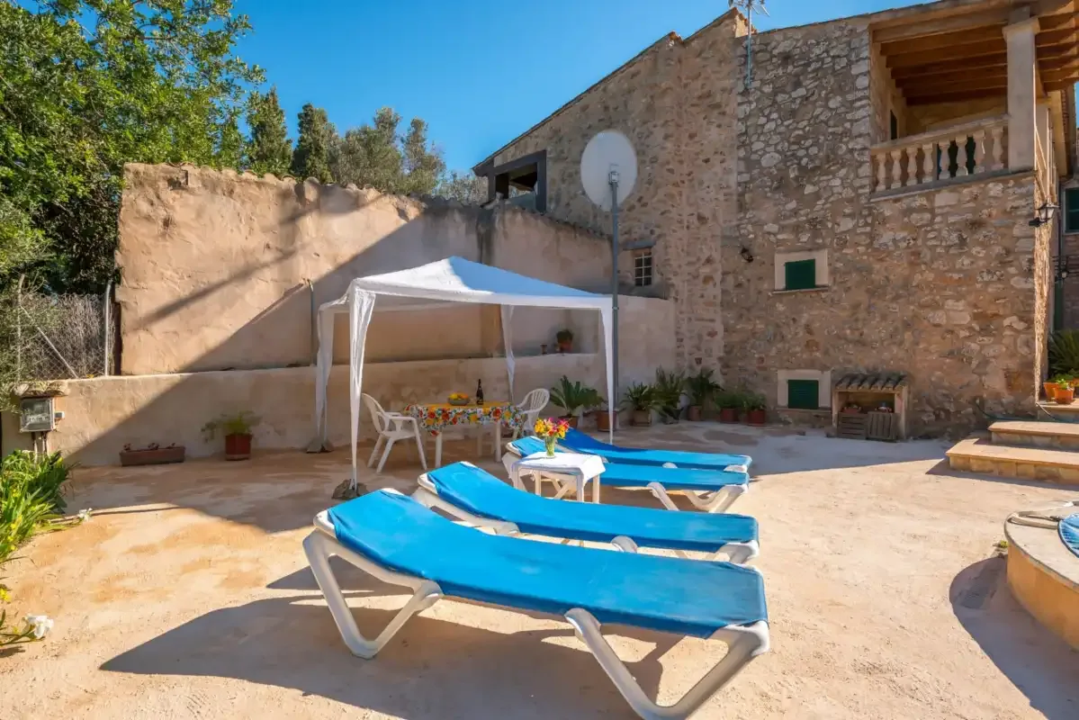 Un patio soleado con tumbonas azules y una zona de estar sombreada junto a un edificio de piedra.