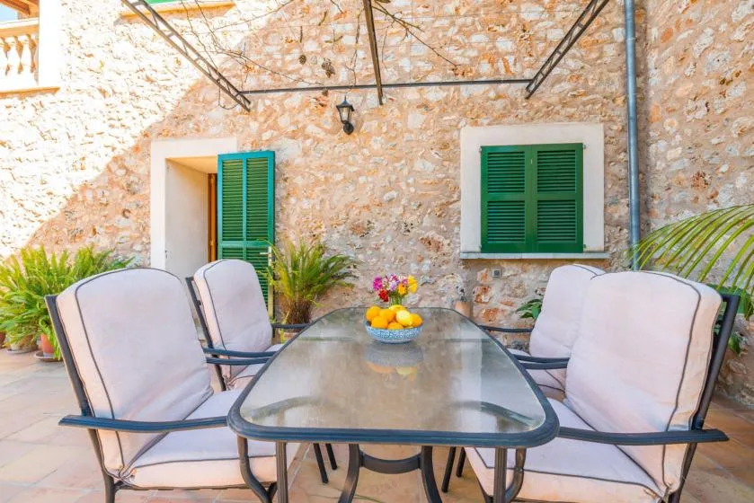 Una zona de comedor en un patio exterior con asientos acolchados y una mesa con superficie de vidrio.
