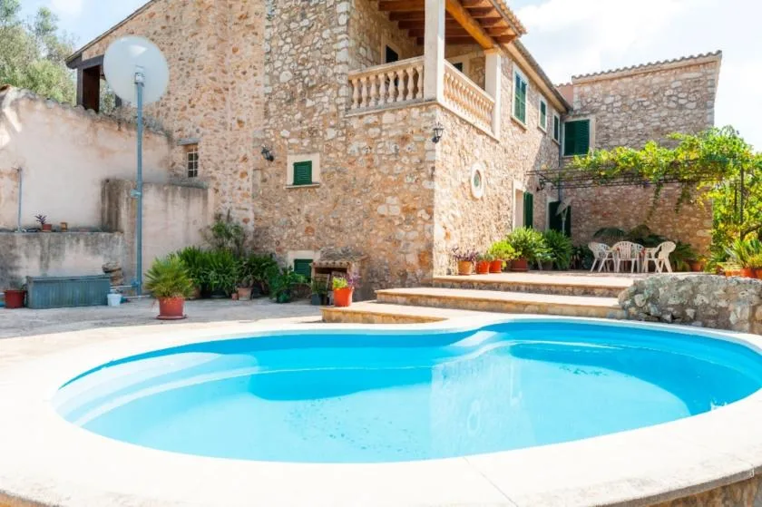 Una piscina está frente a una casa de piedra y un patio.