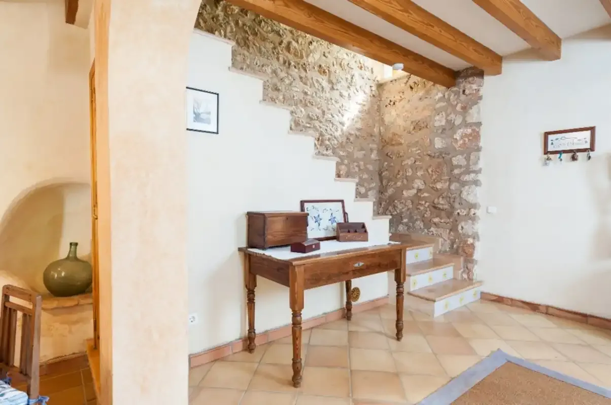 Un interior luminoso con una mesa de madera bajo una escalera y vigas vistas en el techo.
