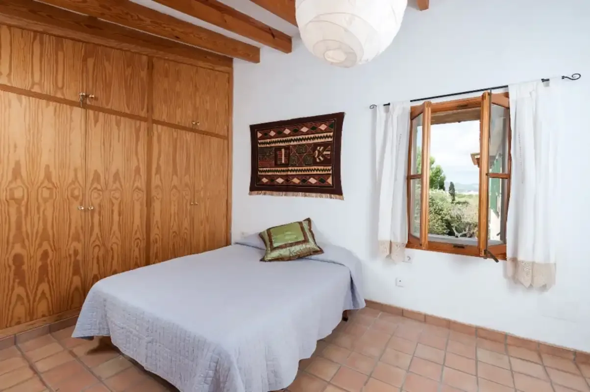 Un dormitorio con una cama junto a un armario de madera y una ventana abierta.