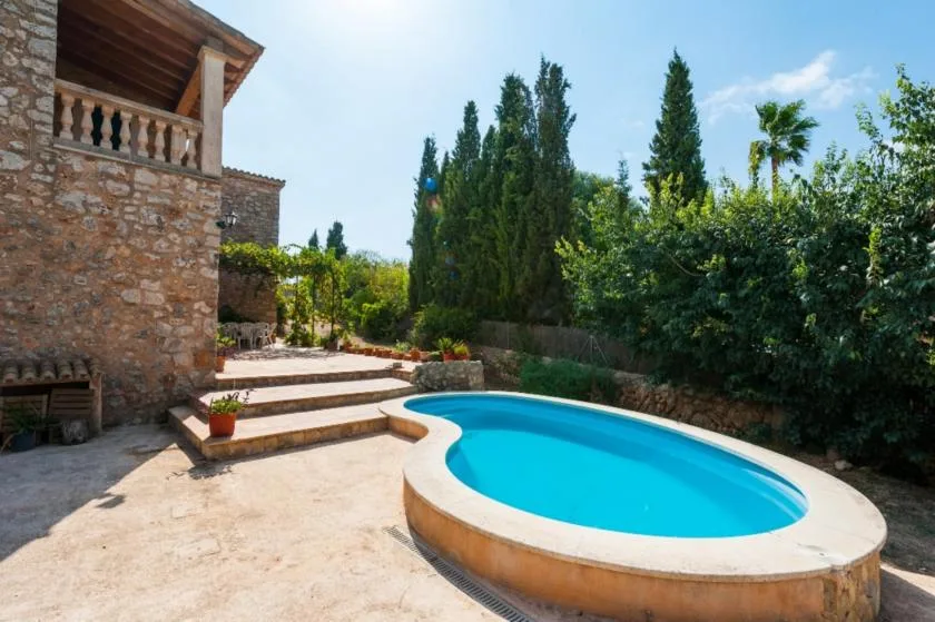 Una piscina al aire libre junto a un edificio de piedra, rodeada de árboles y arbustos.