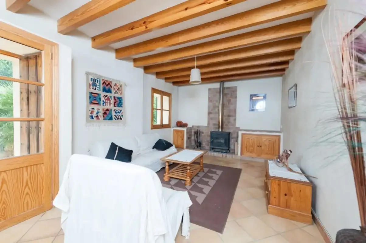 Un salón luminoso con asientos blancos, una mesa de centro y una estufa de leña.