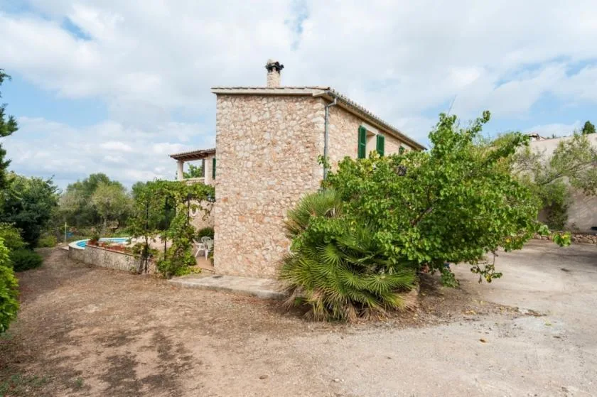 Una casa de piedra se encuentra entre árboles junto a un camino de grava.