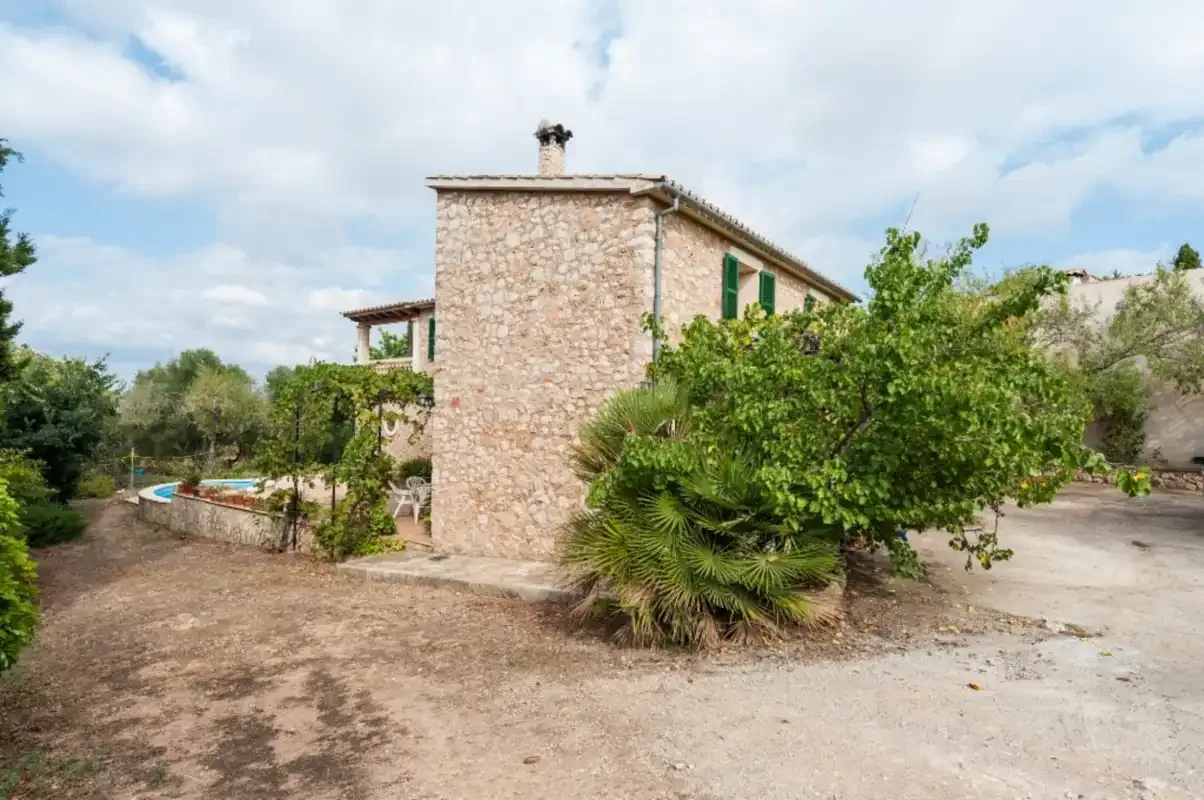 Una casa de piedra está entre árboles junto a un camino pavimentado.