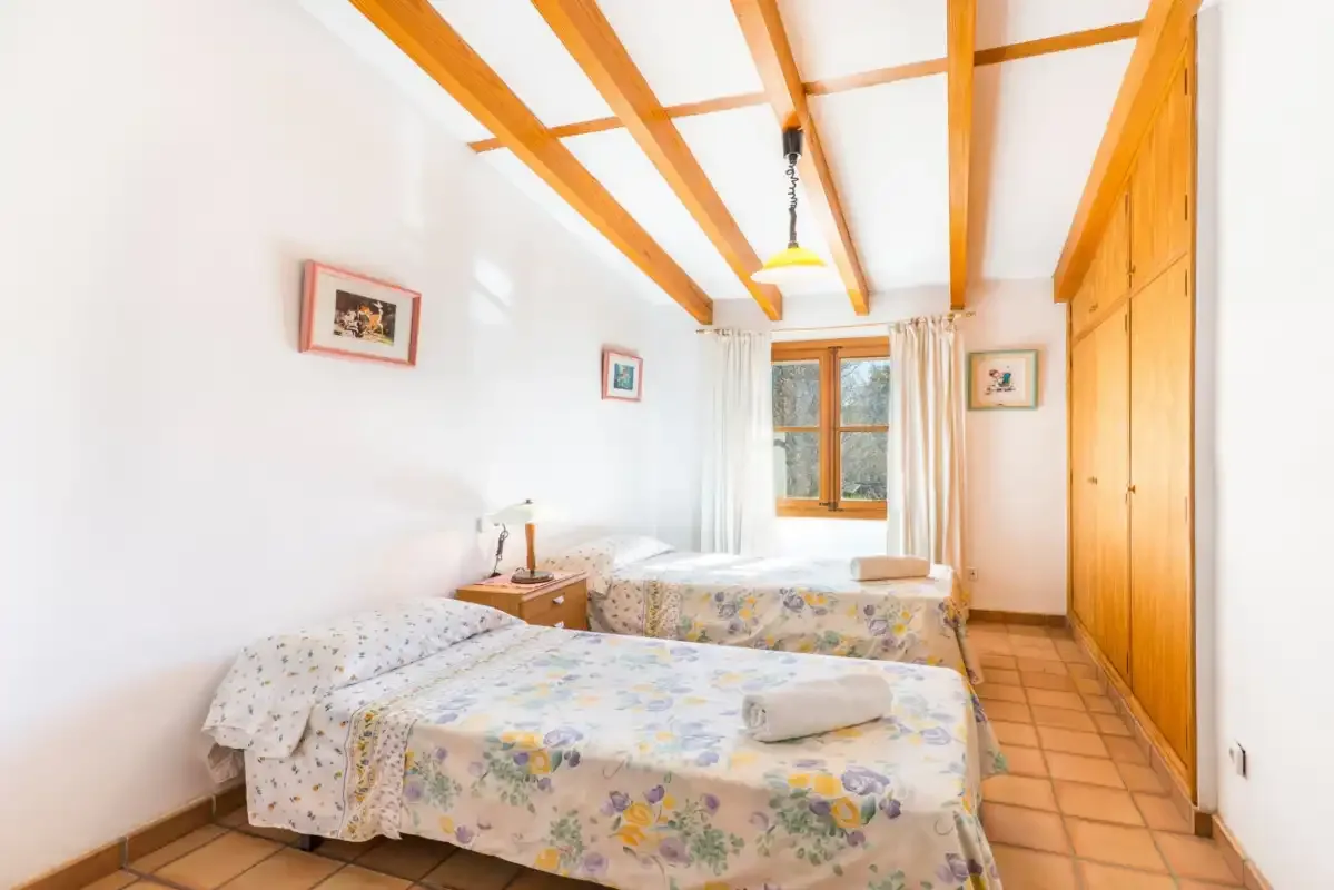 Un dormitorio luminoso con camas, vigas de madera a la vista y un armario.