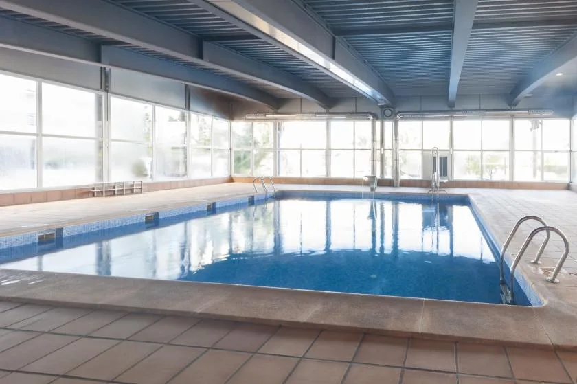 An indoor swimming pool with large windows and a metal ladder.