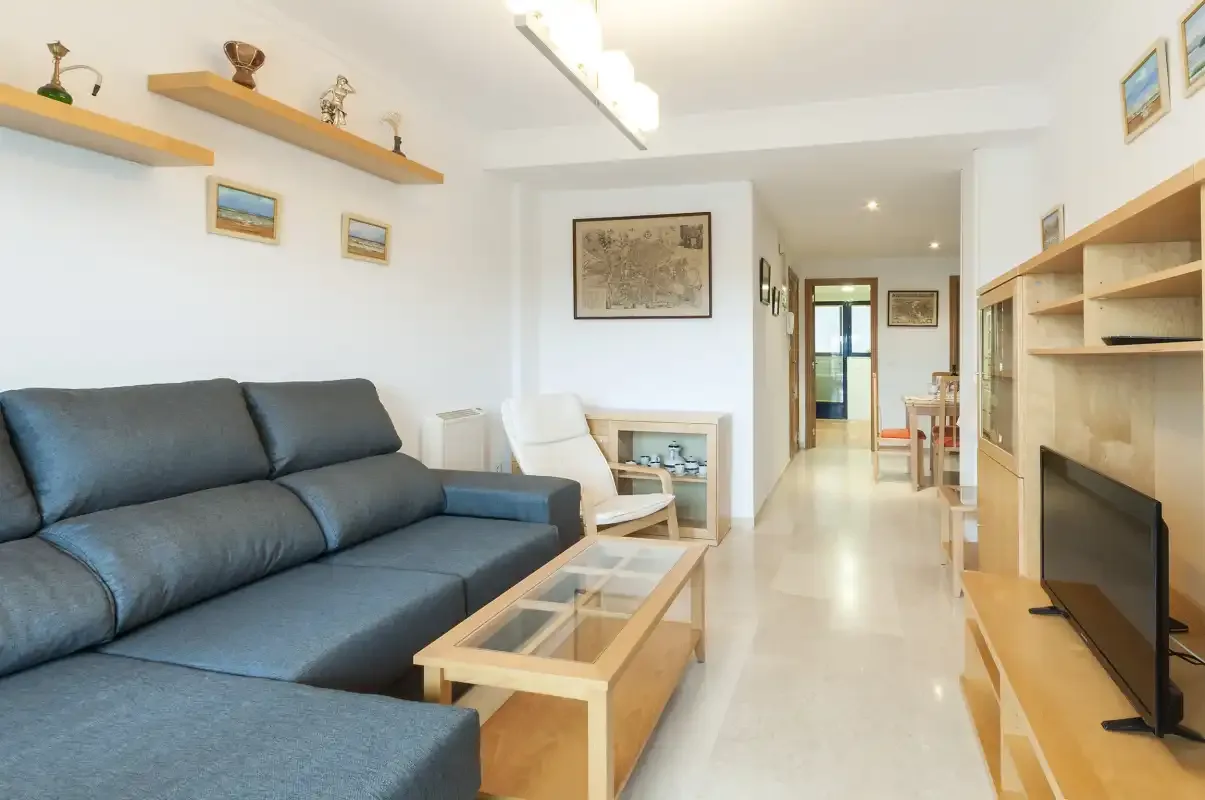 A bright living room with seating, glass-topped tables, and a television.