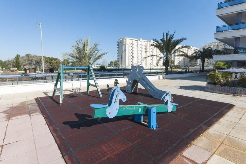 A small playground with a seesaw and slide on a paved outdoor area.