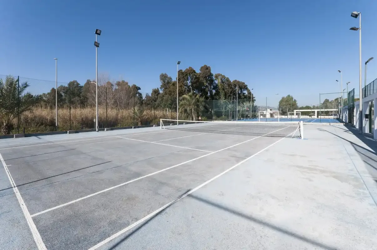 Outdoor sports court with a net, surrounded by trees and light poles.
